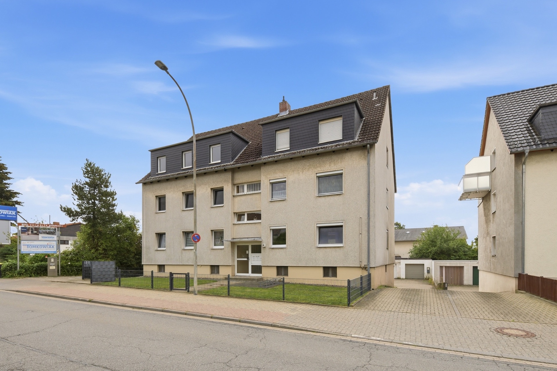Wohngebäude mit drei Etagen, dunklem Dach und Vorgarten, an einer ruhigen Straße gelegen.