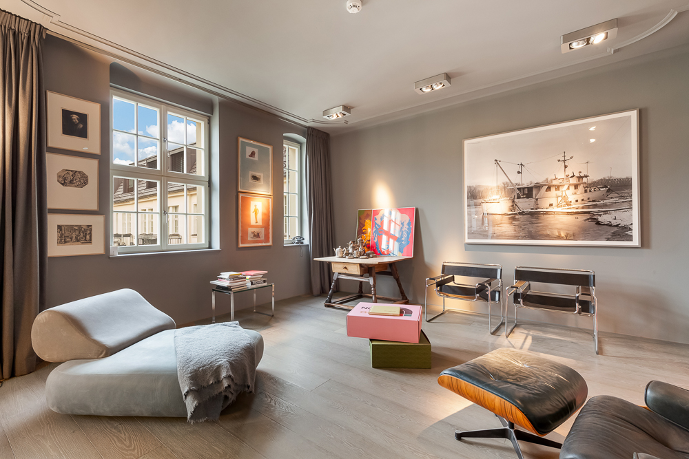 Modernes Wohnzimmer mit grauen Wänden, Sesseln, Kunstwerken und großem Fenster.