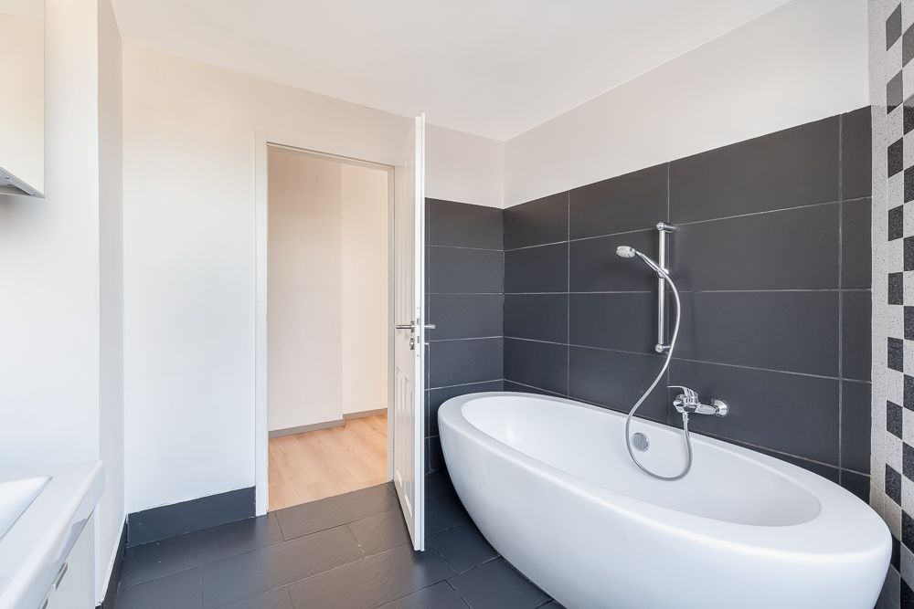 Modernes Badezimmer mit freistehender Badewanne und dunklen Fliesen an der Wand.