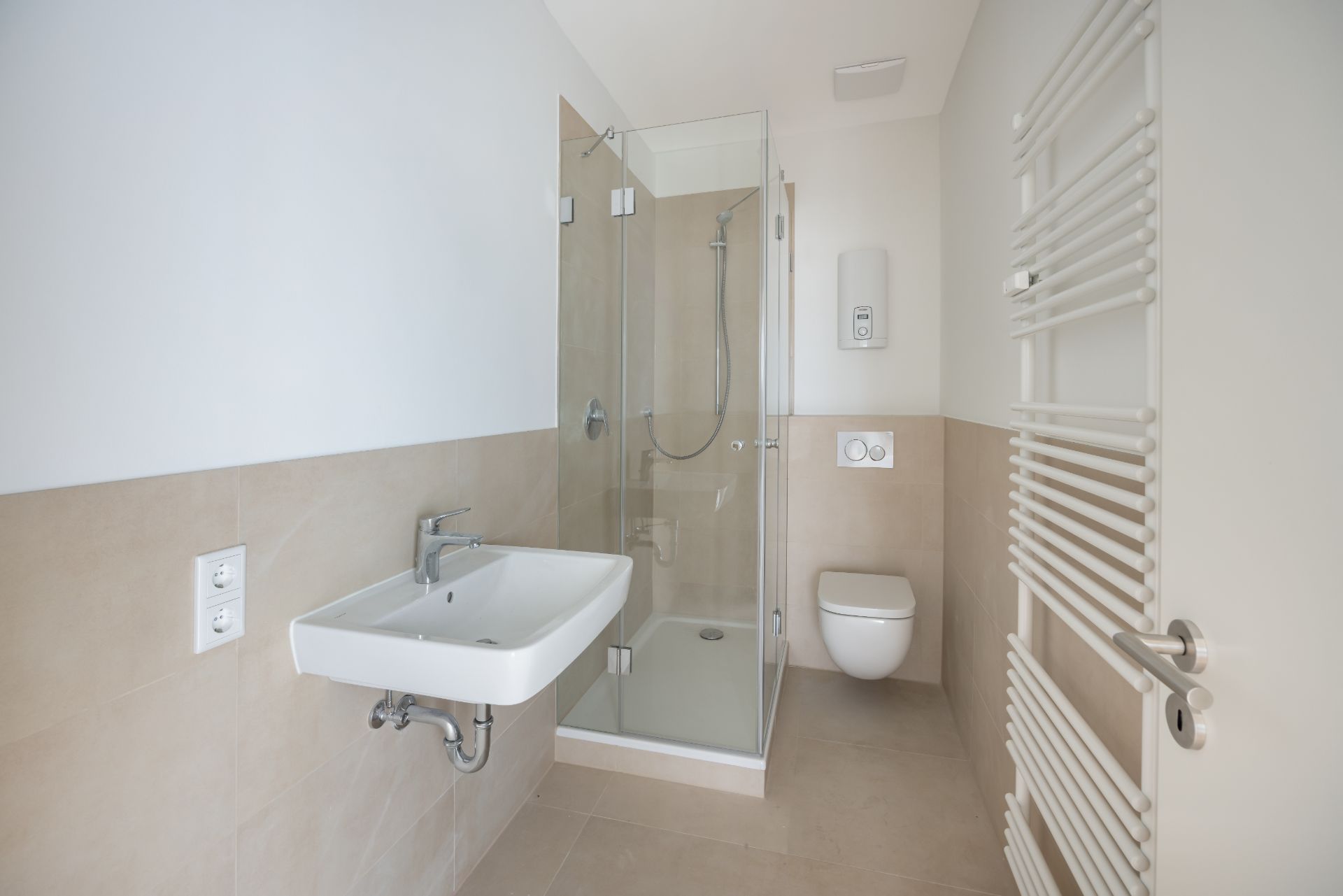 Helles Badezimmer mit Dusche, Wandwaschbecken, WC und Handtuchheizkörper.