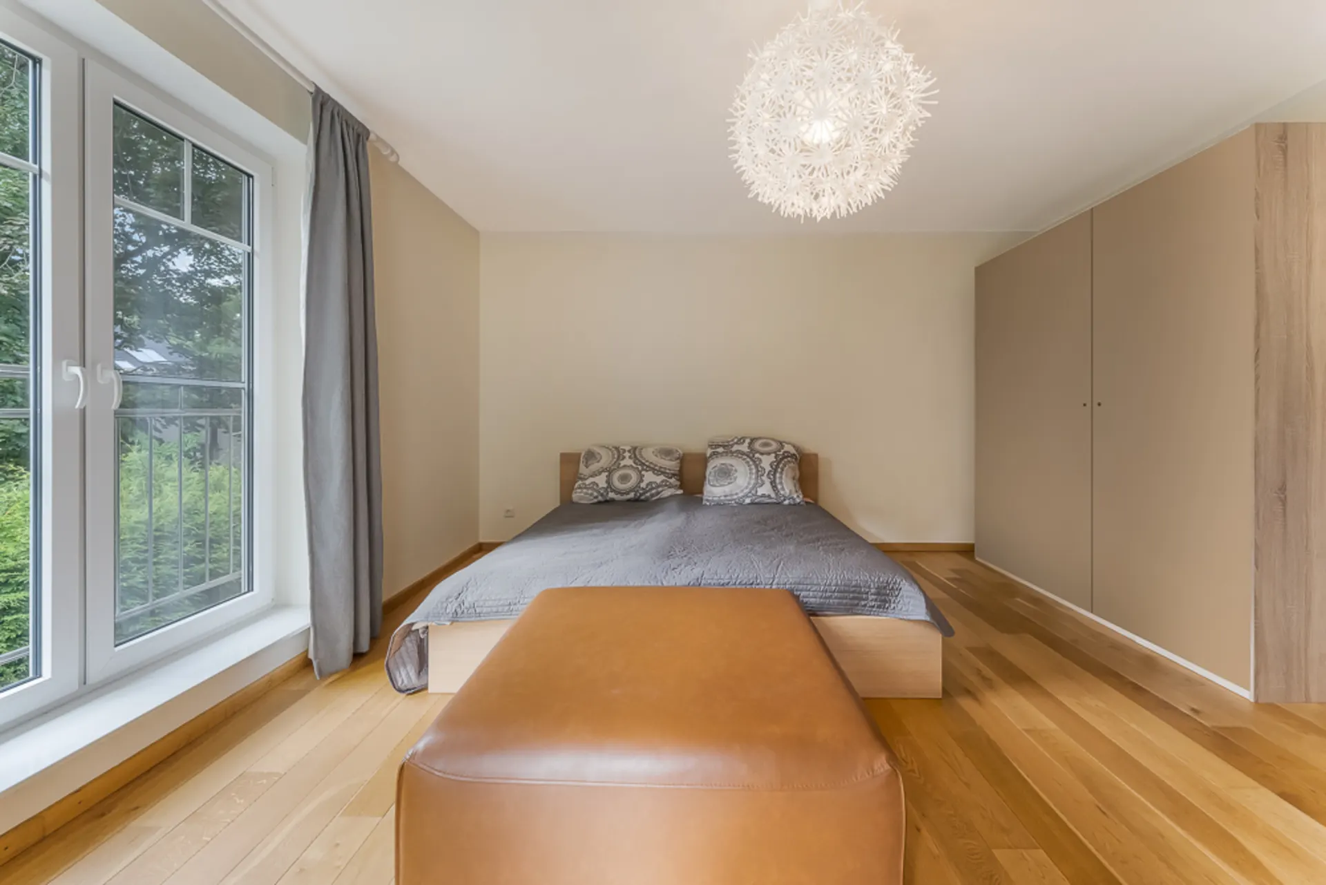 Schlafzimmer mit Doppelbett, großem Fenster, Kleiderschrank und moderner Deckenlampe.