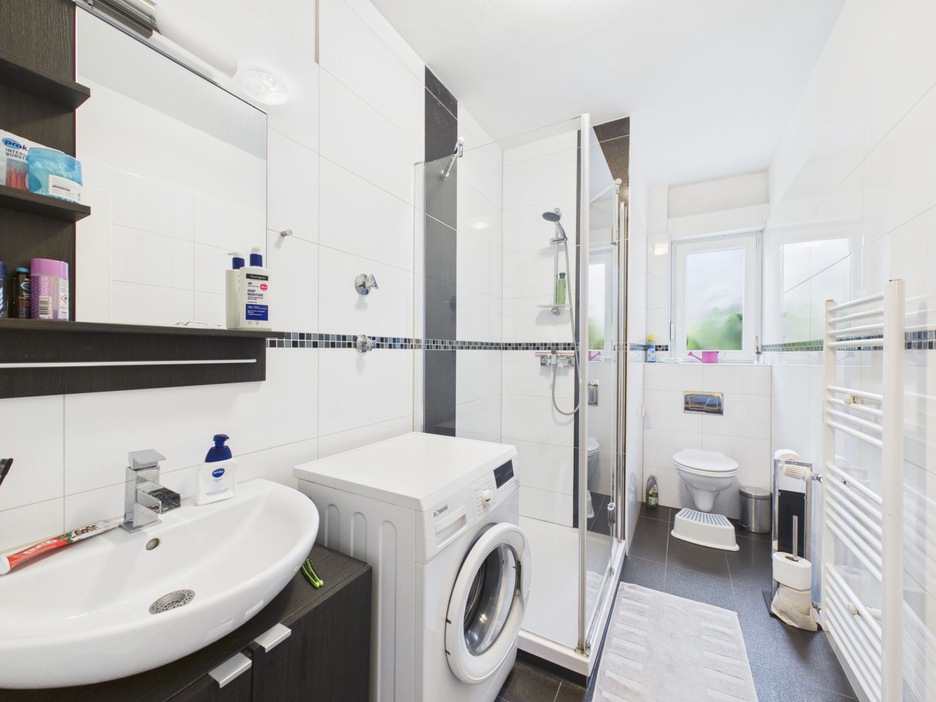 Modernes Badezimmer mit Waschmaschine, Dusche, Waschbecken, WC und Fenster.