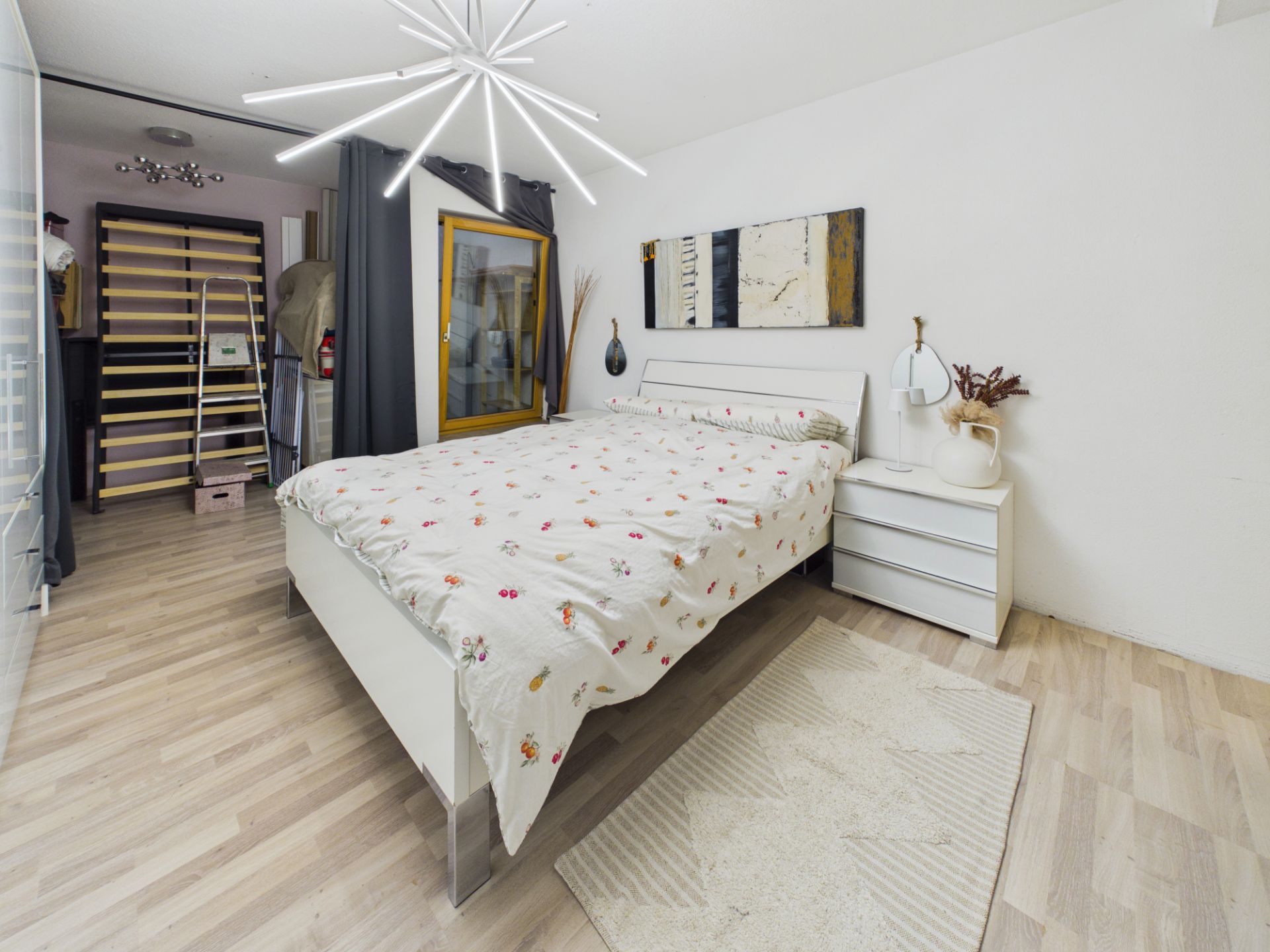 Schlafzimmer mit Doppelbett, Nachttisch, moderner Lampe und abstraktem Bild an der Wand.