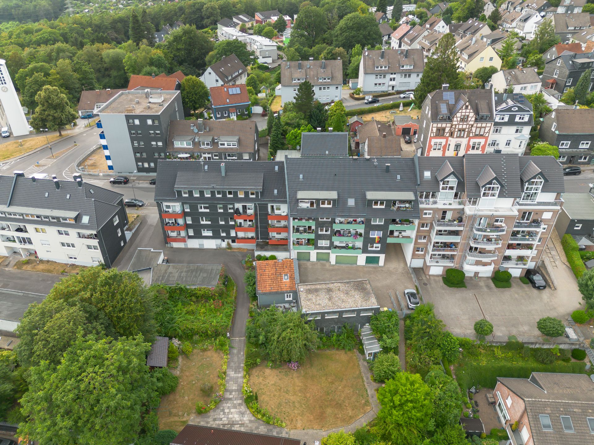 Luftaufnahme von Wohnhäusern mit Balkonen und grünen Gärten im Vordergrund.