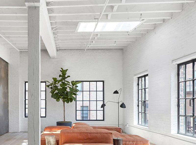 Sala luminosa con sofás naranjas, ventanas grandes, planta y lámpara de pie.