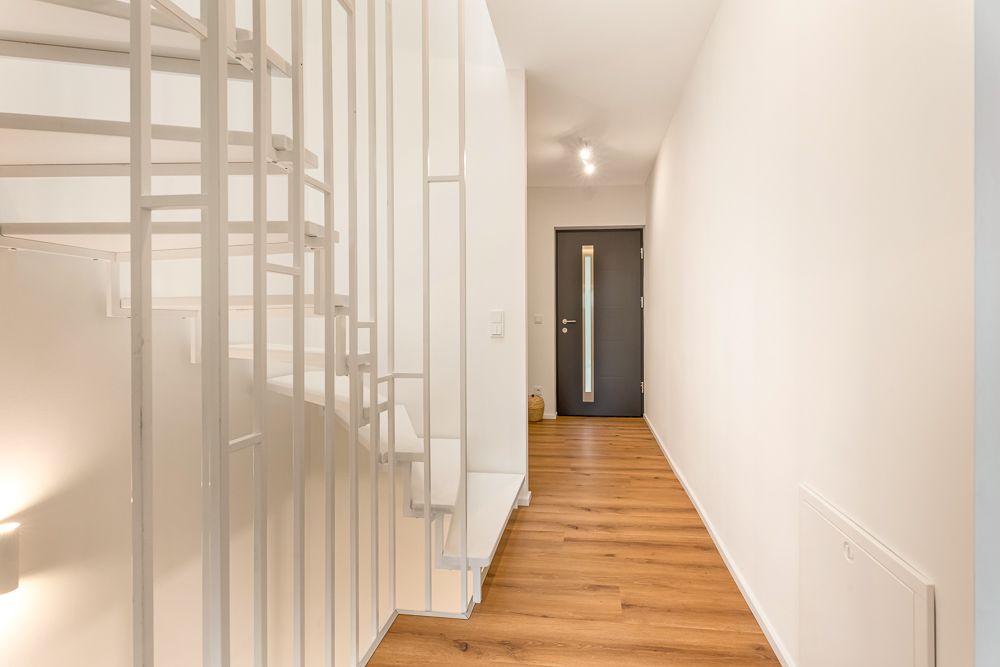 Heller Flur mit Holzfußboden, weißer Wendeltreppe und grauer Haustür.