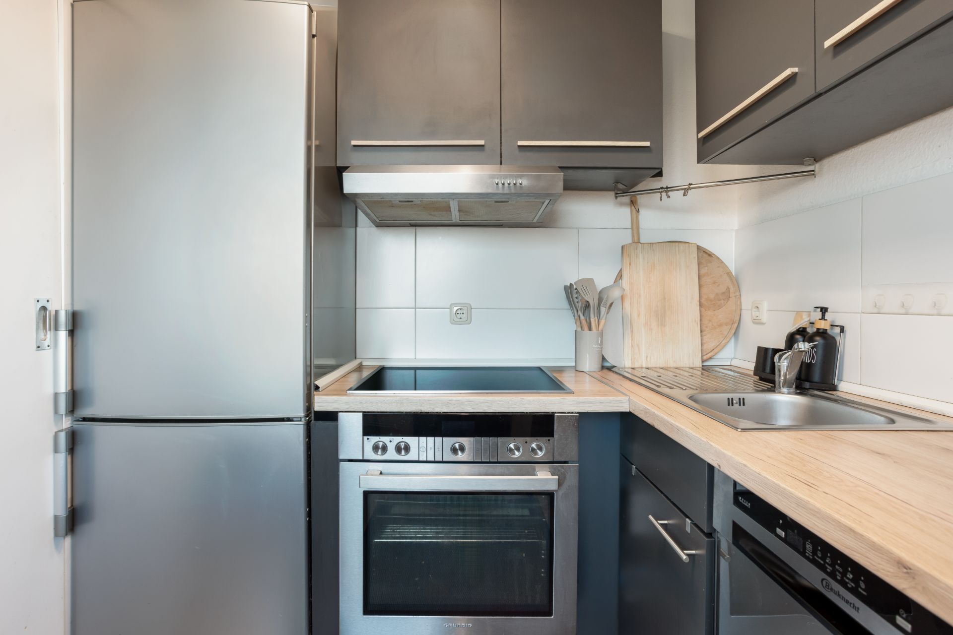 Moderne Küchenecke mit Herd, Kühlschrank, Spüle und grauen Schränken.