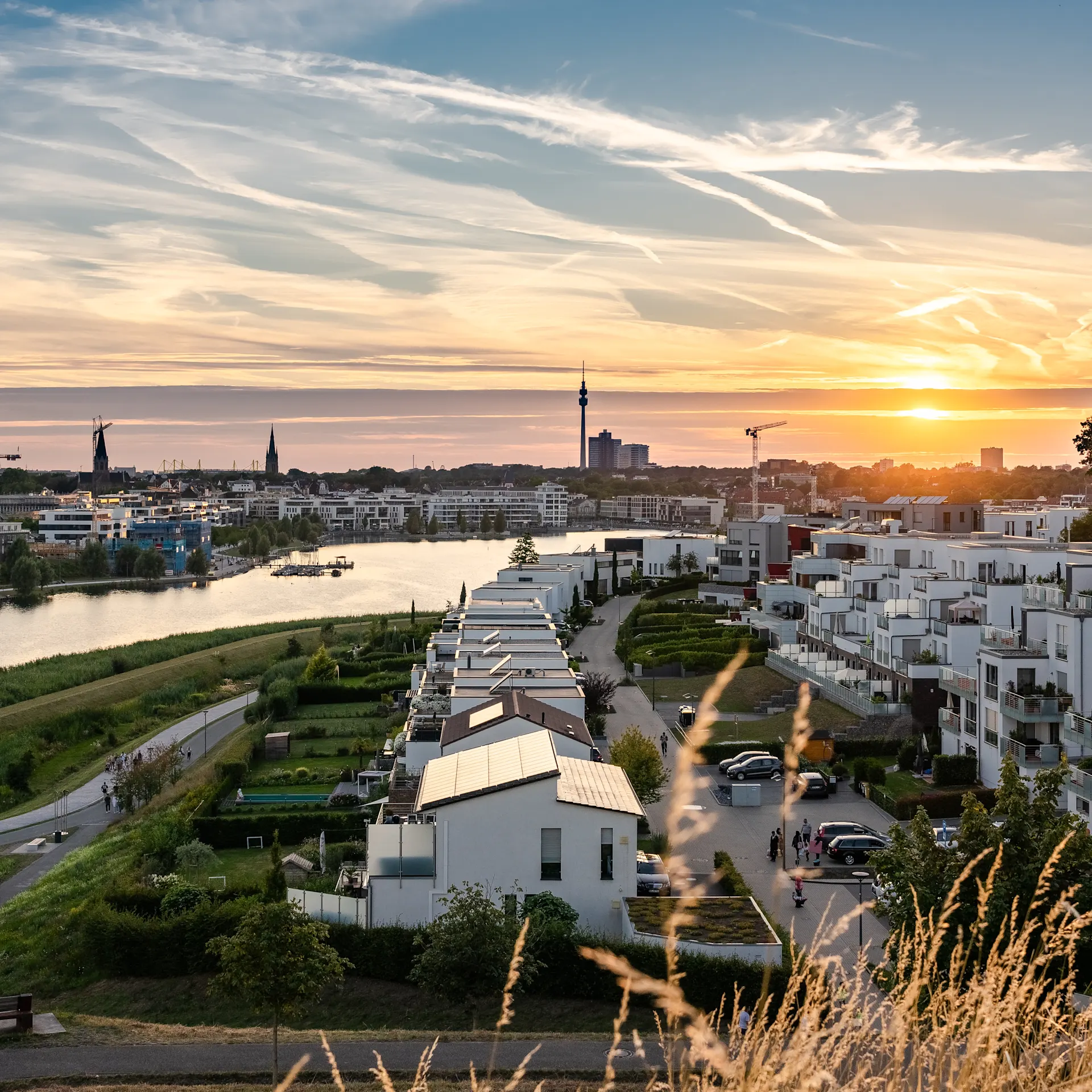 Moderne Wohngebäude am Flussufer bei Sonnenuntergang, mit Blick auf die Stadt im Hintergrund.
