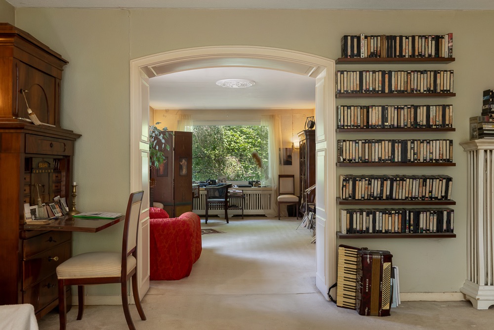 Wohnzimmer mit roten Sesseln, Bücherregalen und großem Fenster mit Blick ins Grüne.