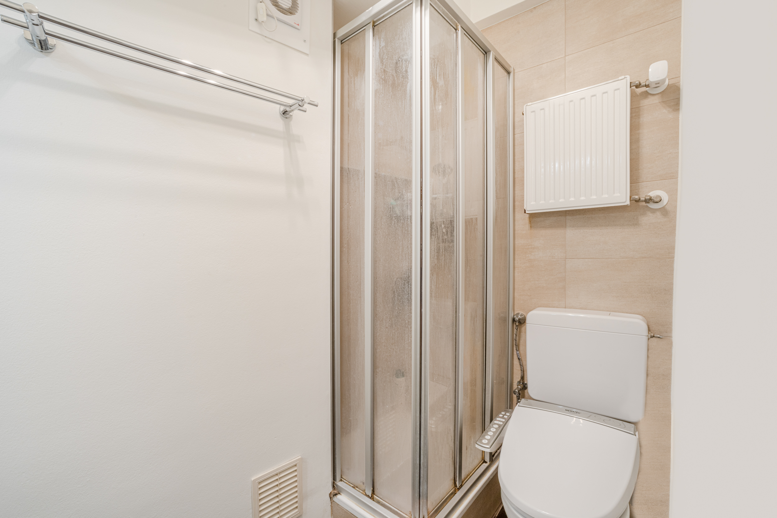 Kleines Badezimmer mit Duschkabine, Toilette und Handtuchhalter an der Wand.