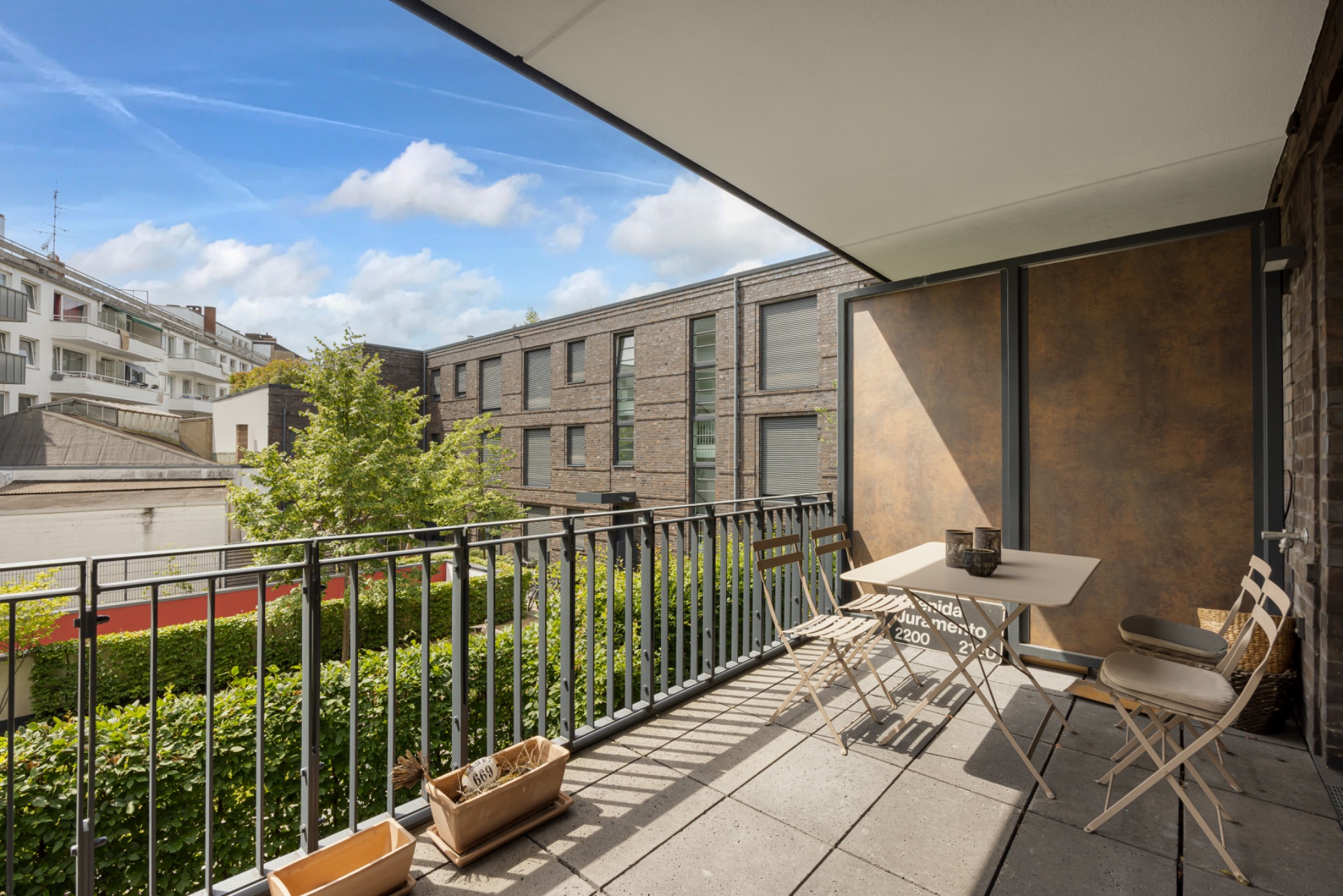 Überdachter Balkon mit Tisch und Stühlen, Blick auf benachbarte Gebäude und Grünanlage.