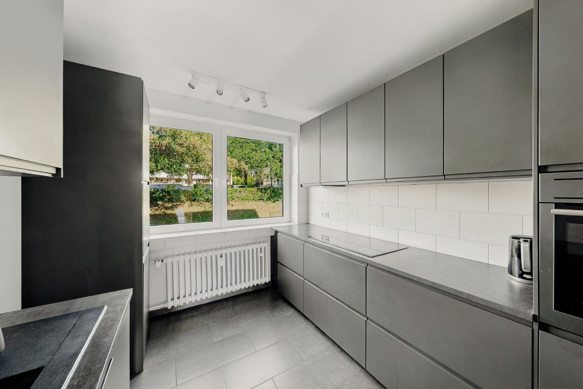Moderne Küche mit grauen Schränken, großem Fenster und weißen Fliesen an der Wand.