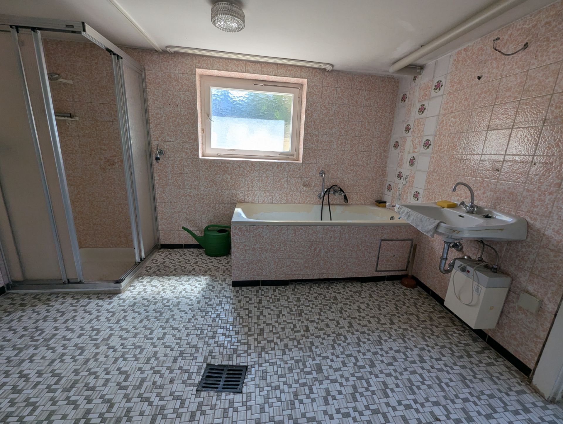 Badezimmer mit Badewanne, Dusche, Waschbecken und Fenster, auf hell gemustertem Fliesenboden.
