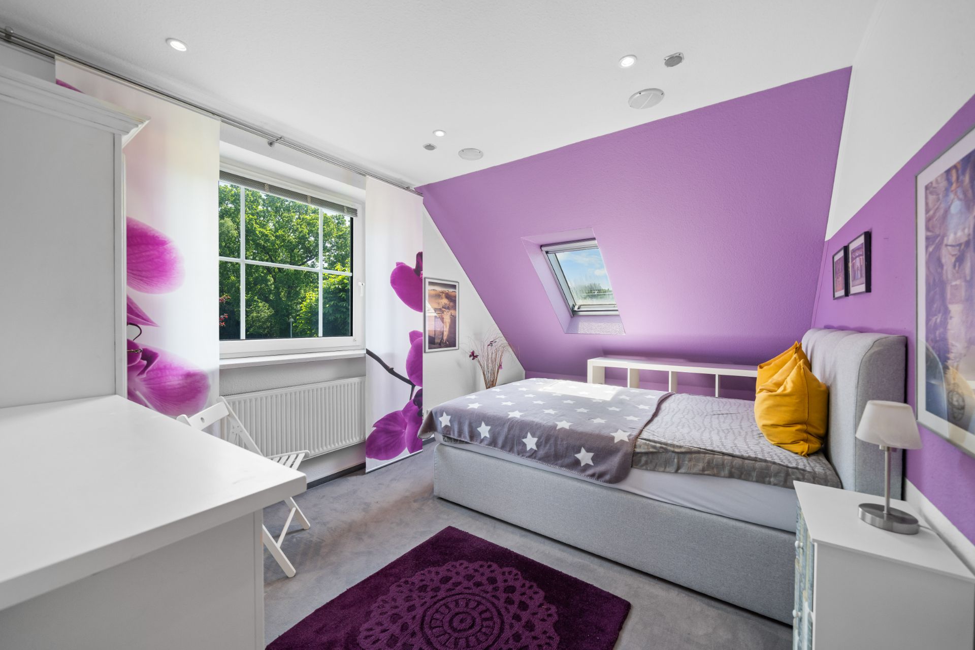 Helles Schlafzimmer mit lila Wand, Bett, Fenster und dekorativen Elementen.