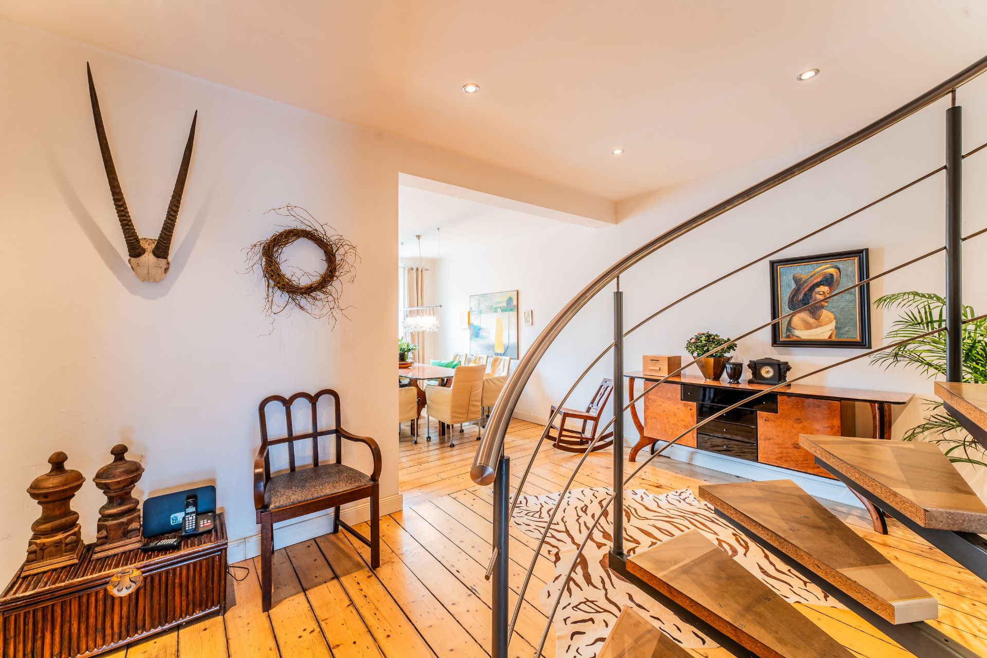 Heller Flur mit Holztreppe, Holzboden, Kommode, Bild, Dekorationen und Blick ins Esszimmer.