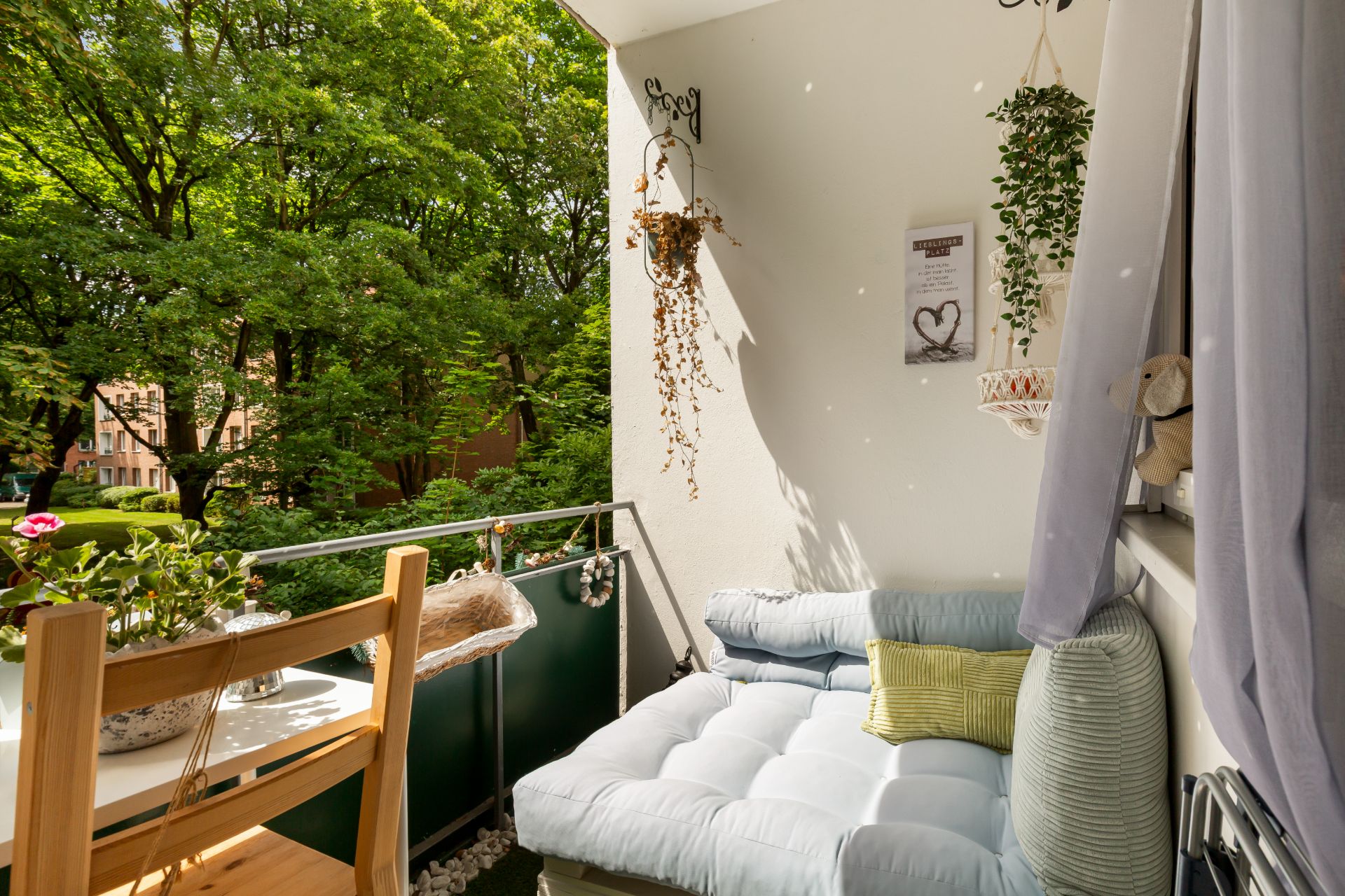 Gemütlicher Balkon mit Sofa, Tisch, Stühlen und Pflanzen, umgeben von grünen Bäumen.