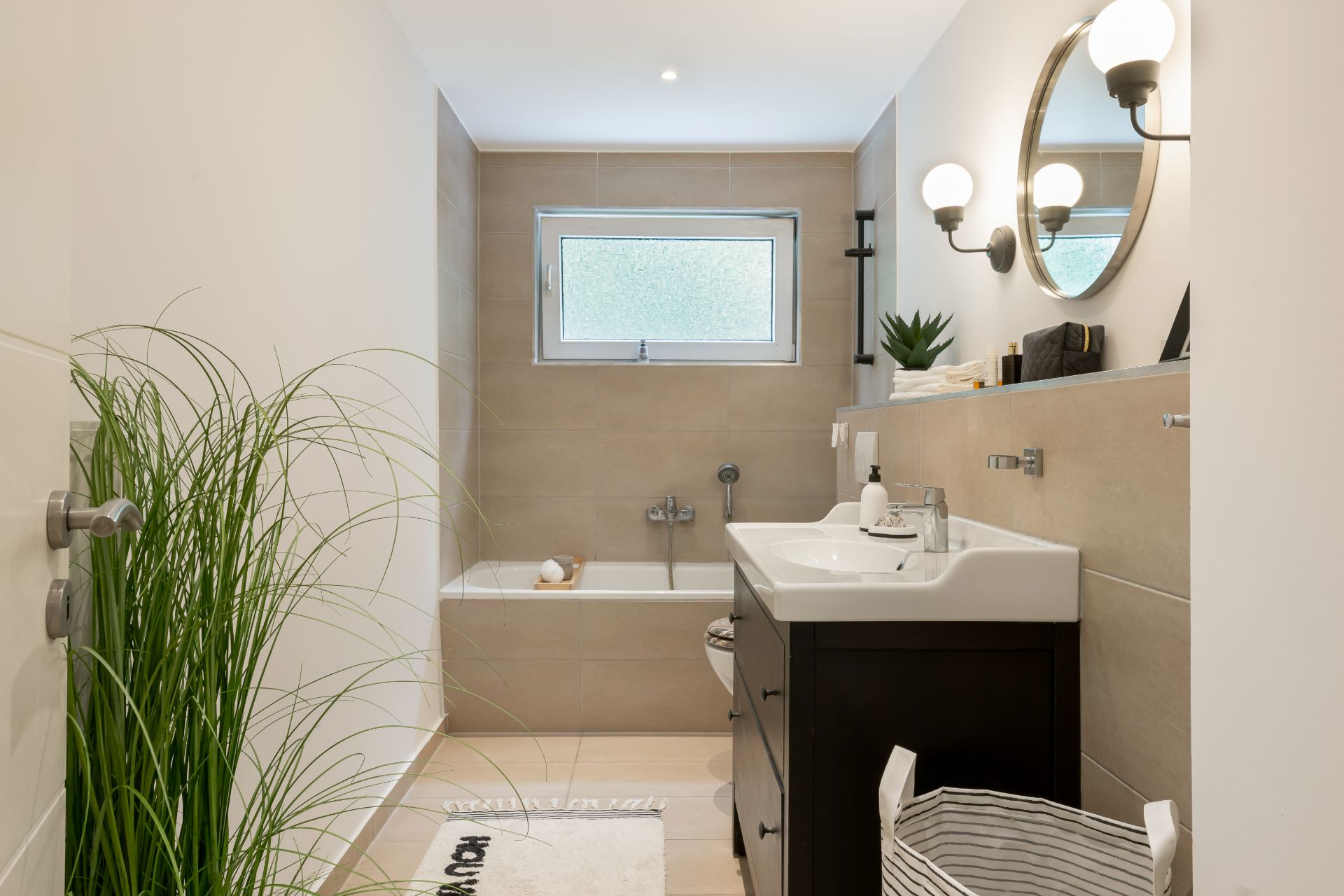 Modernes Badezimmer mit Badewanne, Waschbecken, Spiegel und Pflanzen.