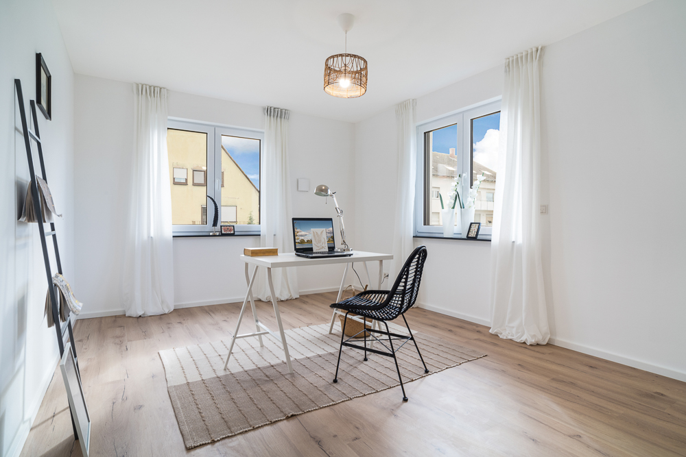 Helles Arbeitszimmer mit Schreibtisch, Stuhl und großen Fenstern, auf Holzfußboden.