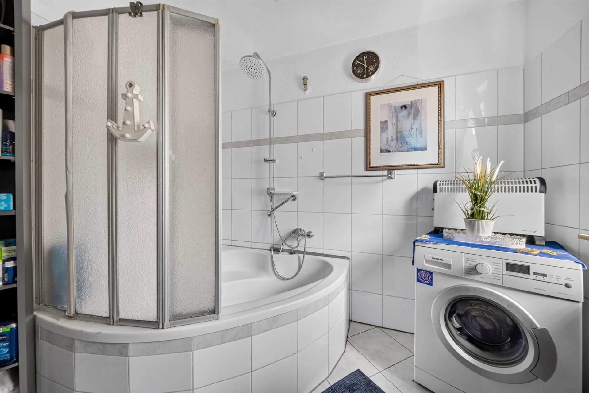Badezimmer mit Eckbadewanne, Duschwand, Waschmaschine und Pflanze auf dem Gerät.