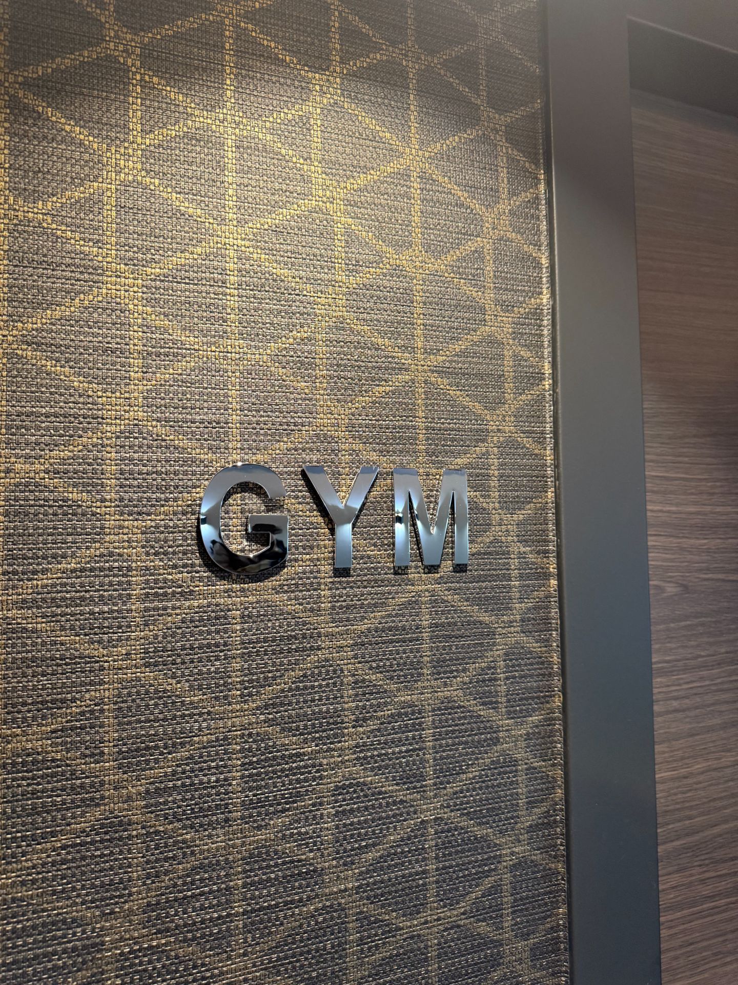 Ein Türschild mit dem Wort 'GYM' auf einer gemusterten Wand.