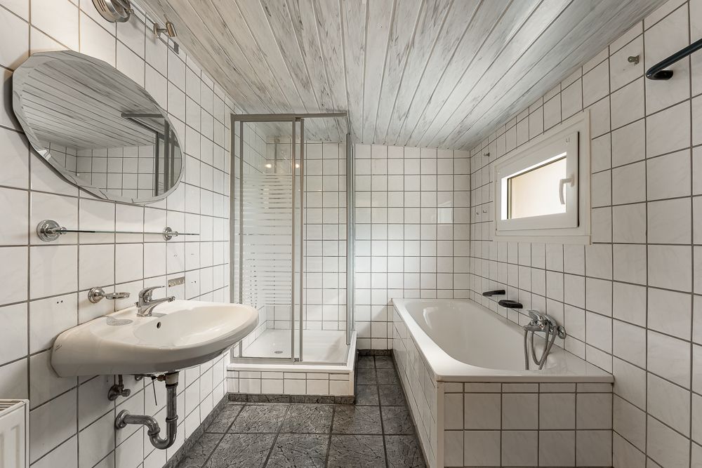 Helles Badezimmer mit Badewanne, Dusche, Waschbecken, Spiegel und kleinem Fenster.