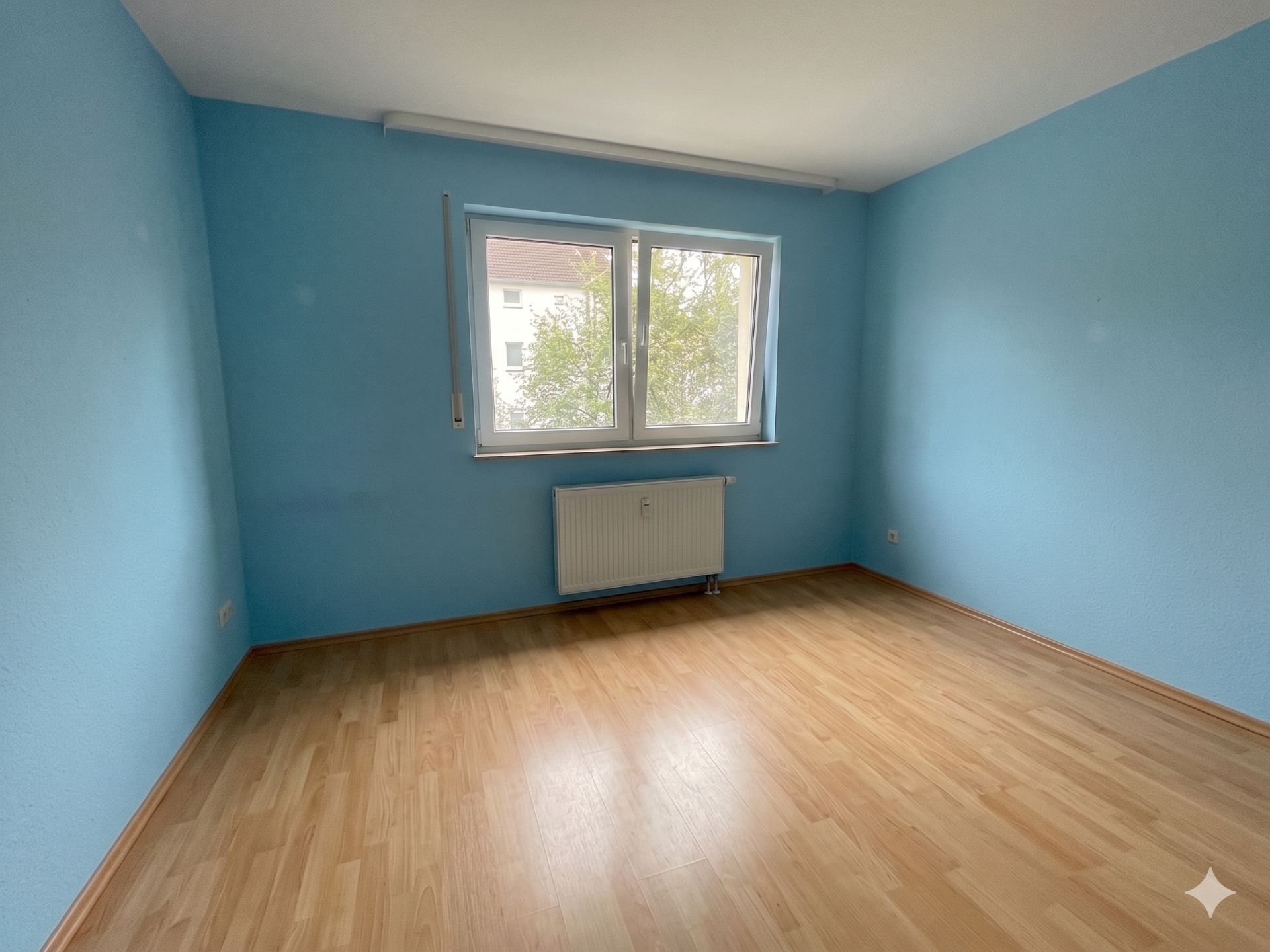 Leerer Raum mit hellblau gestrichenen Wänden, Holzfußboden und Fenster mit Blick nach draußen.