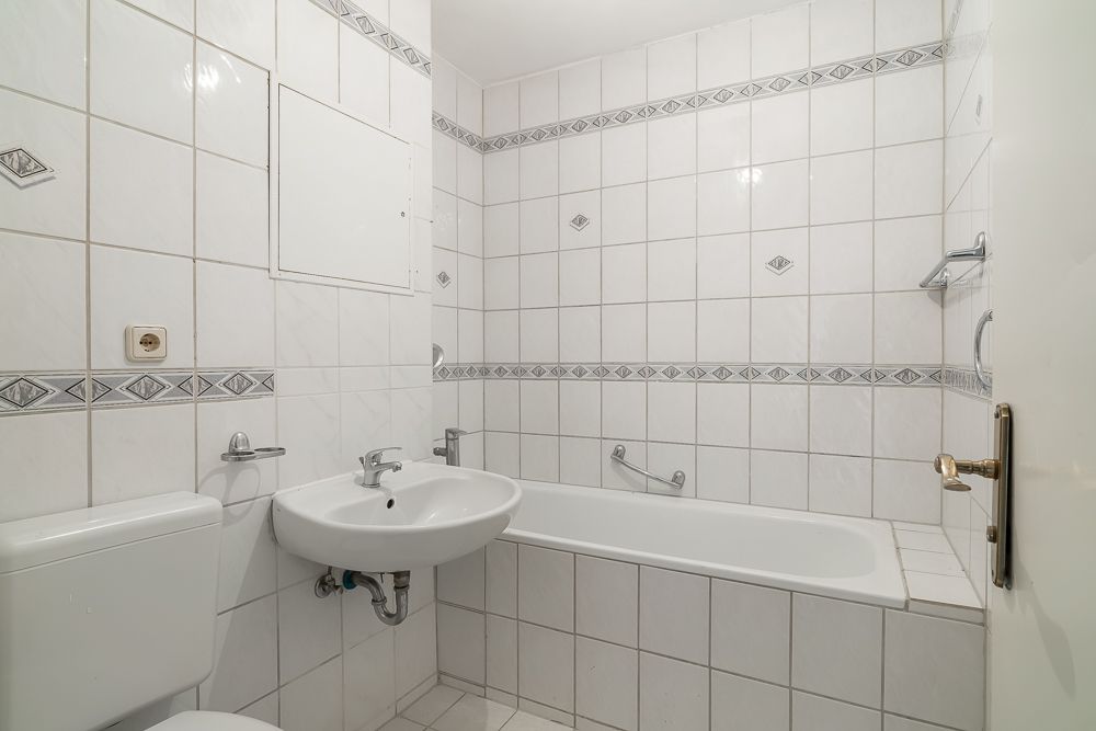 Weiß gefliestes Badezimmer mit Badewanne, Waschbecken und Toilette.