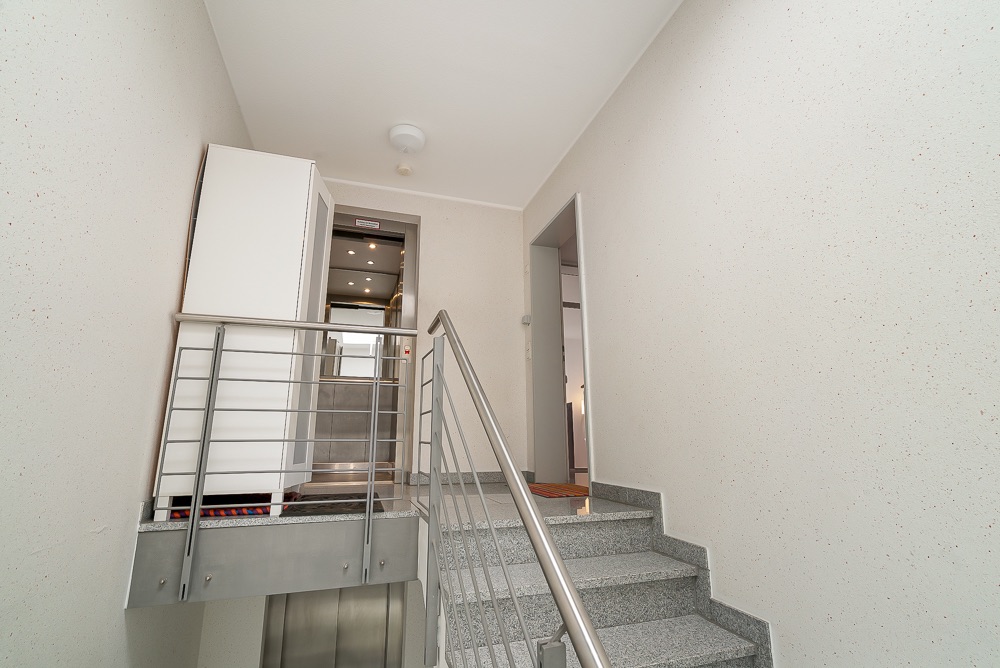 Treppenhaus mit Metallgeländer, Aufzug und Flur in einem Wohngebäude.