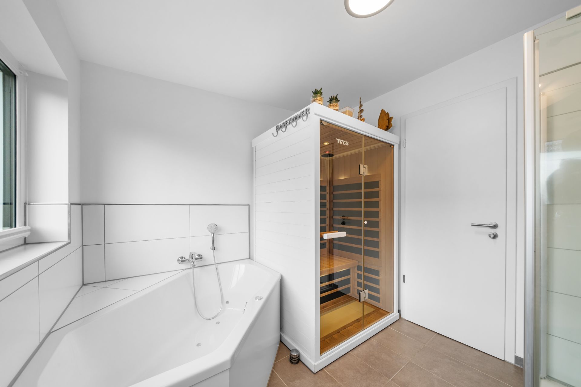 Modernes Badezimmer mit Eckbadewanne und Sauna, daneben eine weiße Tür.