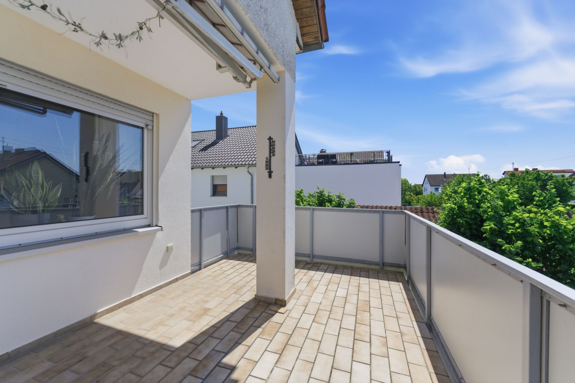 Geräumiger Balkon mit Fliesenboden, Geländer und Blick auf Nachbarhäuser und Bäume.