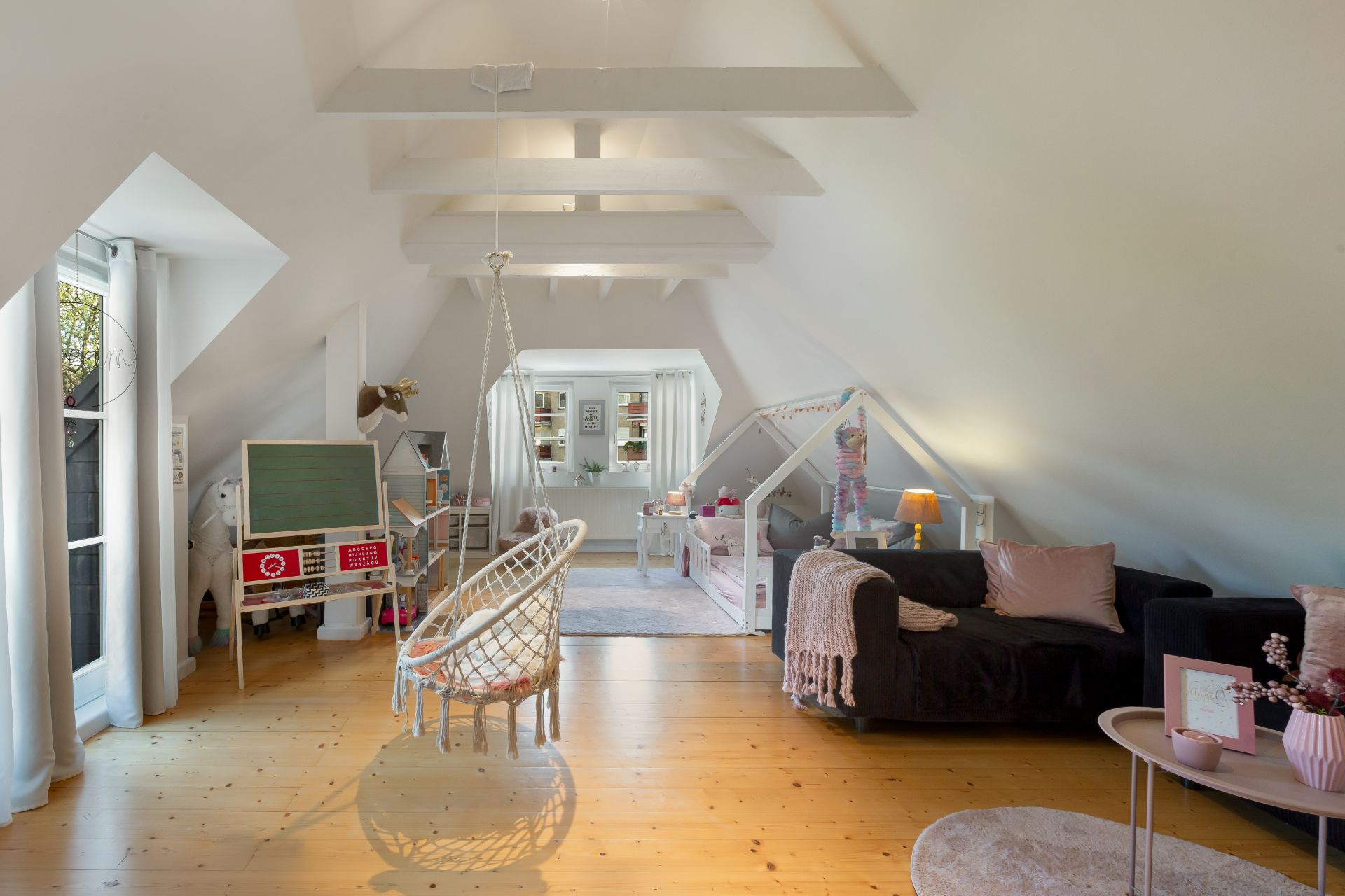 Heller Dachgeschossraum mit Spielbereich, Sofa, Hängesessel und Kinderschreibtisch.