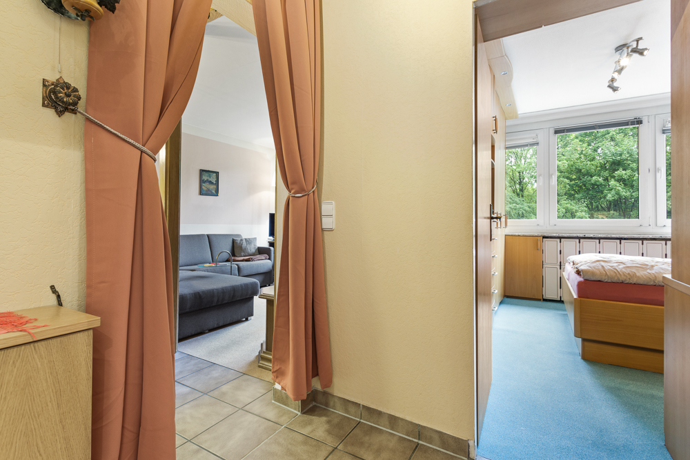 Blick aus dem Flur auf ein Wohnzimmer mit Sofa und ein Schlafzimmer mit großem Fenster.