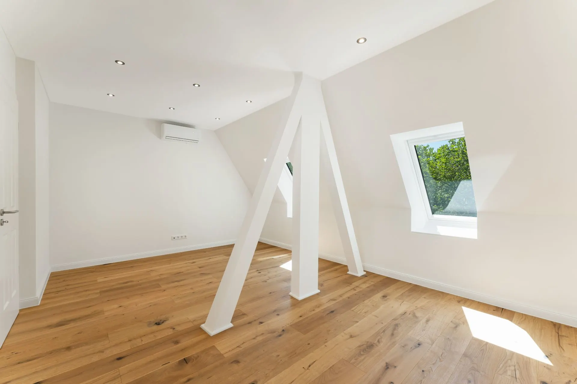 Heller Dachraum mit Holzboden, weißen Wänden, sichtbaren Balken und zwei Fenstern.