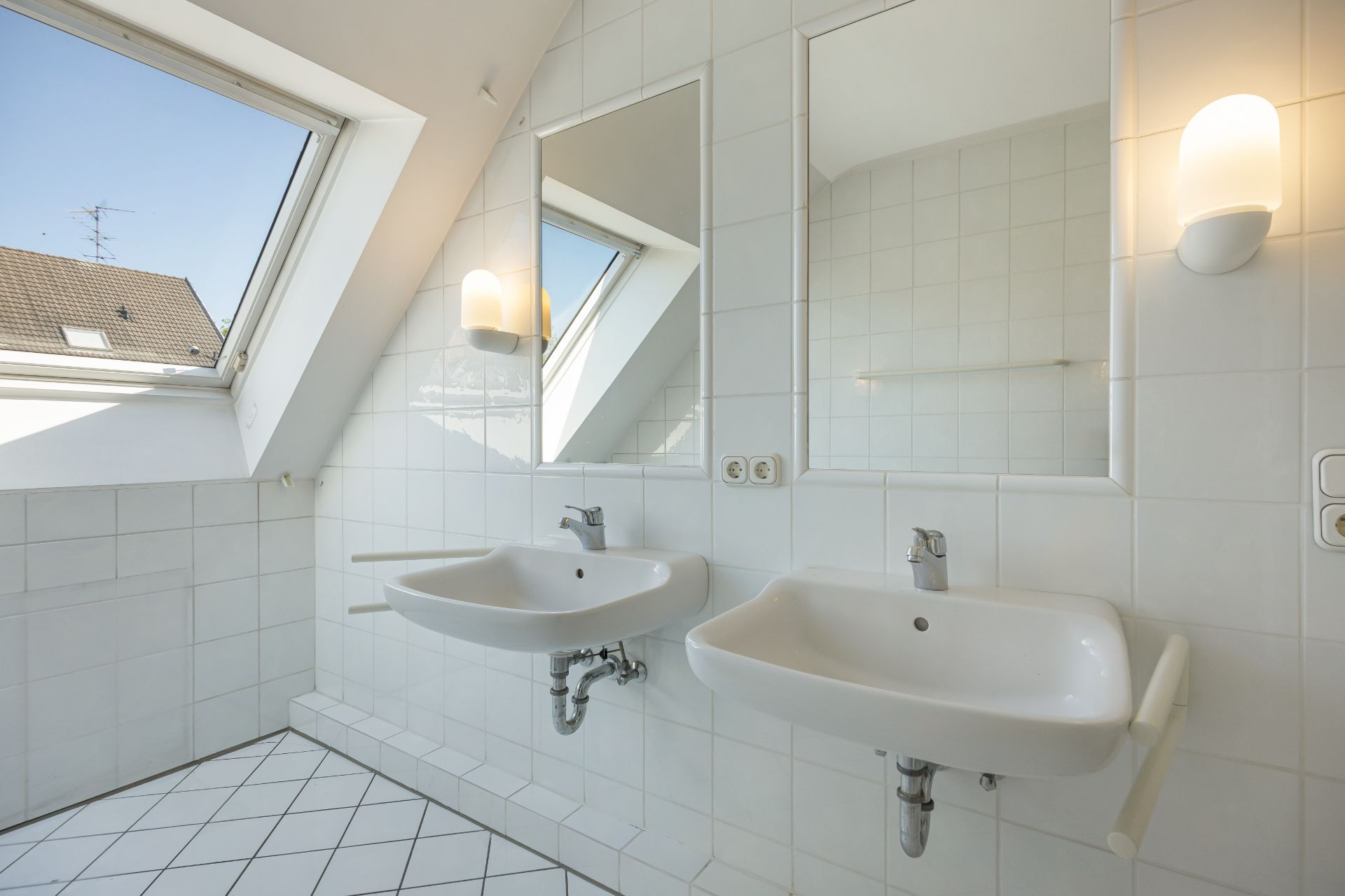 Helles Badezimmer mit zwei Waschbecken, zwei Spiegeln und großen Dachfenstern.