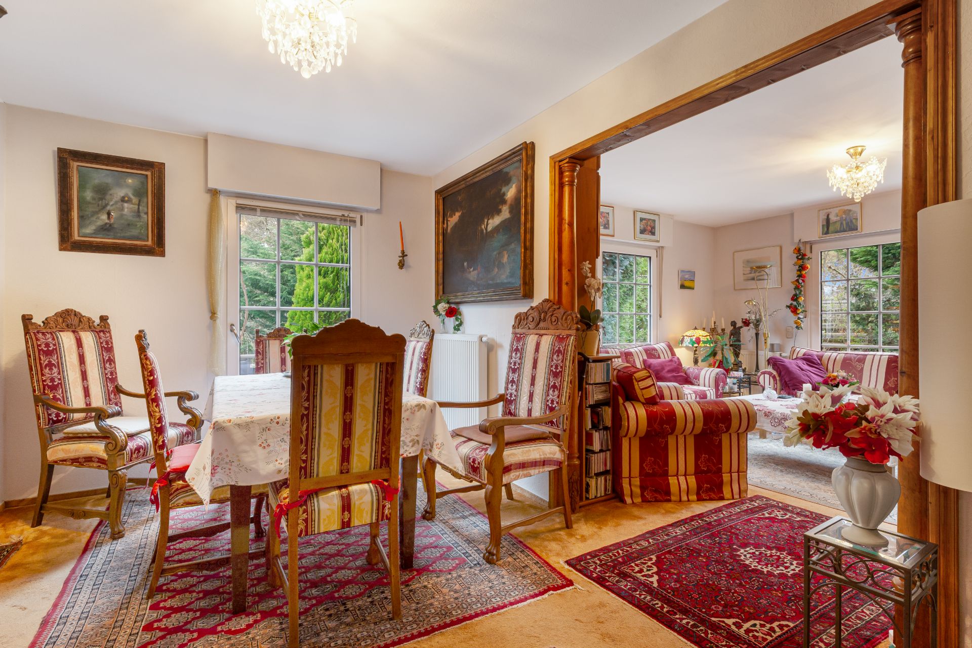 Esszimmer mit Holzmöbeln und Blick ins gemütliche Wohnzimmer, dekoriert mit Teppichen und Bildern.