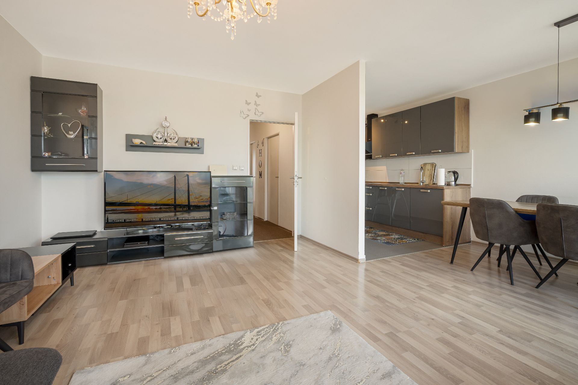 Modernes Wohnzimmer mit TV, offener Küche und Esstisch auf hellem Holzfußboden.