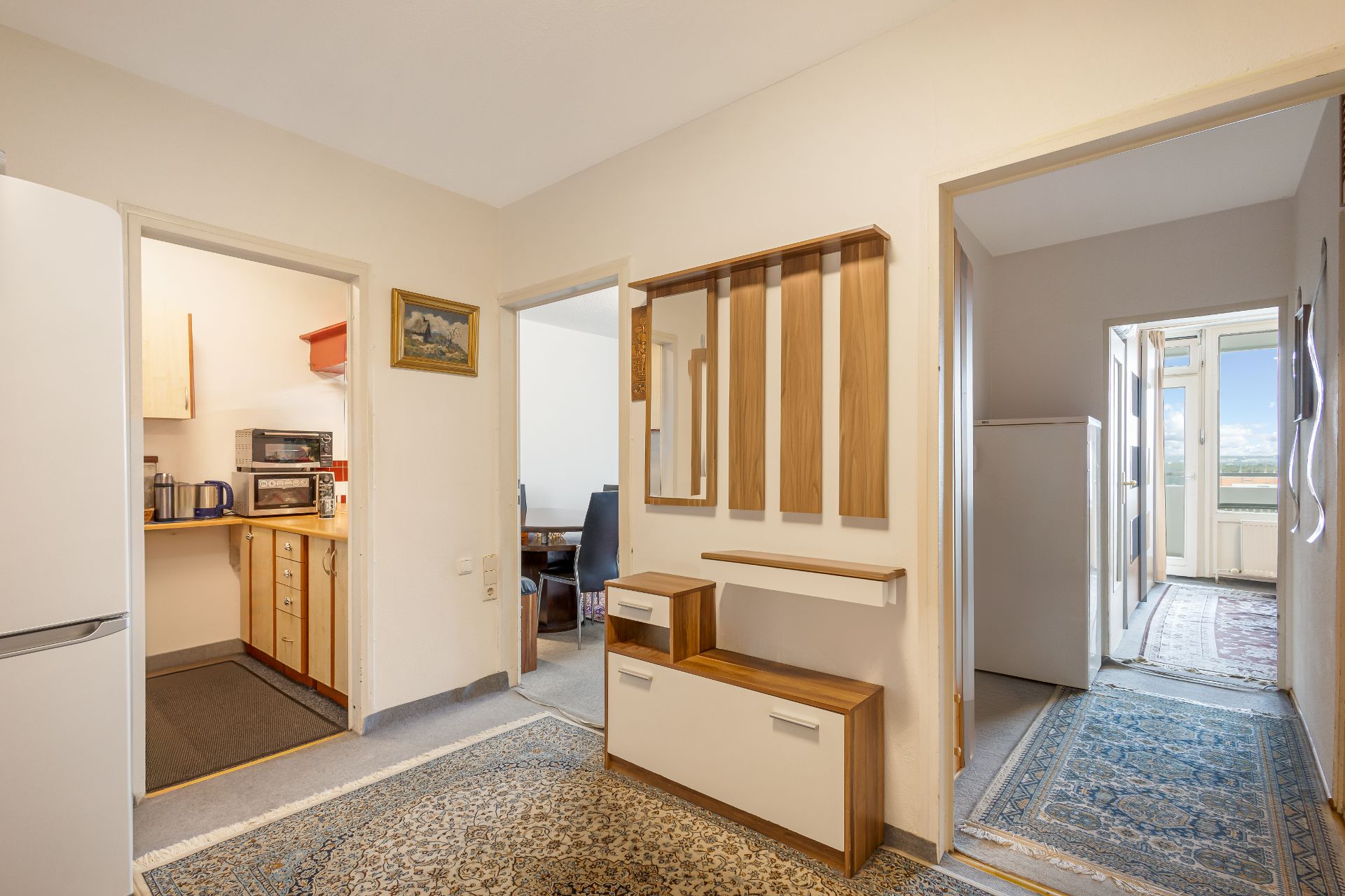 Heller Flur mit Teppich, Garderobe, drei Türen zu Küche, Zimmer und Balkon.