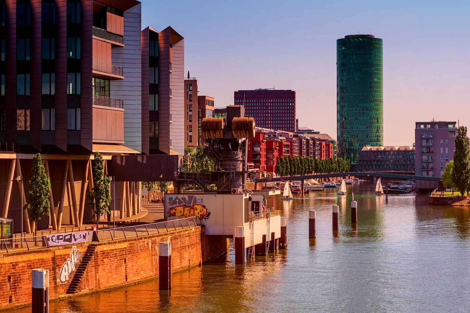 Moderne Wohngebäude am Flussufer mit Booten und Hochhäusern im Hintergrund.