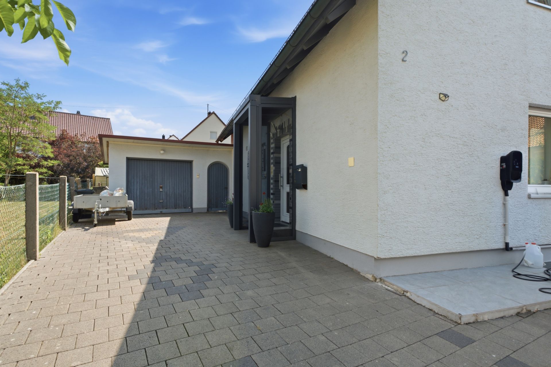 Gepflasterter Hof mit Garage und Eingangstür an einem Wohnhaus bei Tageslicht.