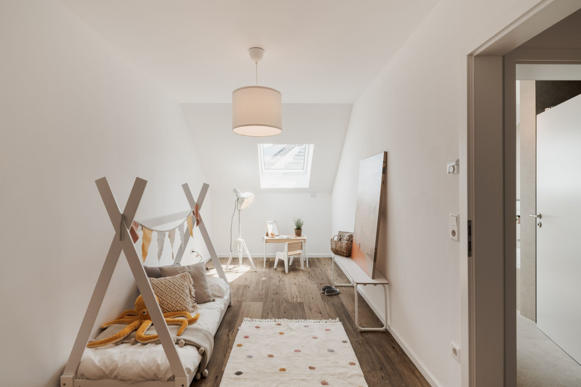 Helles Kinderzimmer mit Holzboden, kleinem Bett, Schreibtisch und Dachfenster.