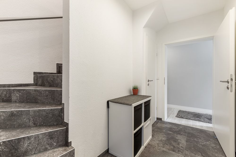 Flur mit grauer Steintreppe, kleinem Regal und Pflanze auf einer Ablage.