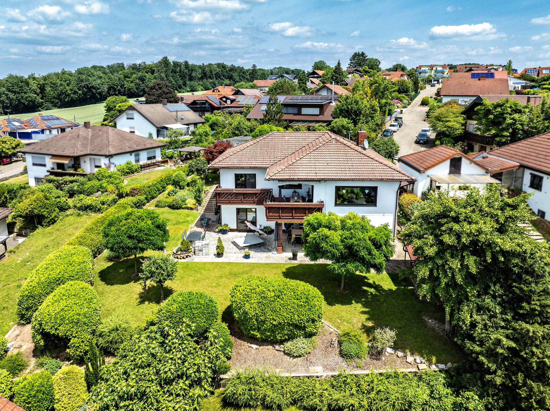 Luftaufnahme eines Einfamilienhauses mit Garten und Terrasse in ruhiger Wohngegend.