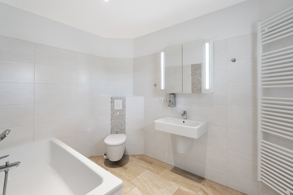 Modernes Bad mit Badewanne, Toilette, Waschbecken und beleuchtetem Spiegel.