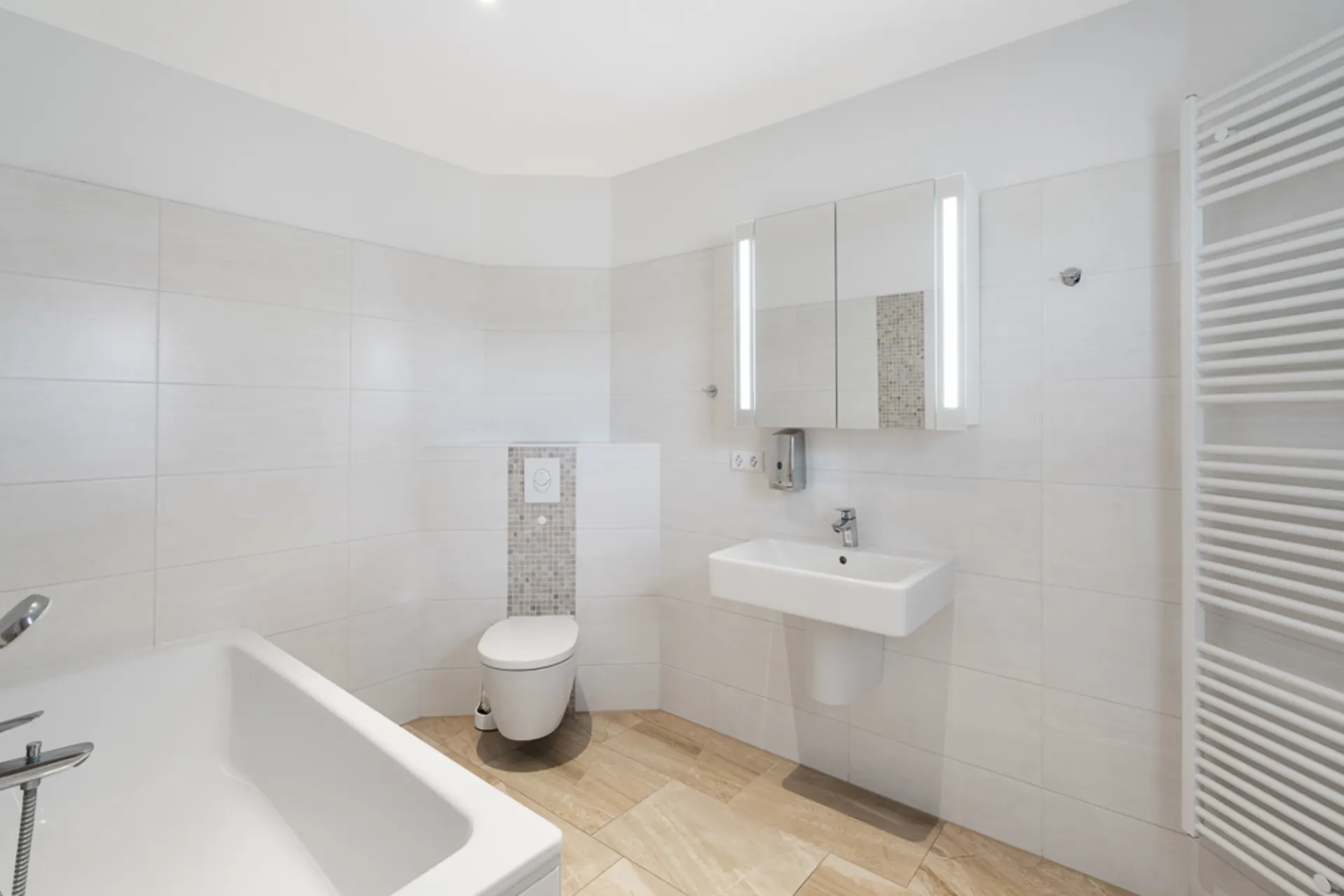 Modernes Bad mit Badewanne, Toilette, Waschbecken und beleuchtetem Spiegel.