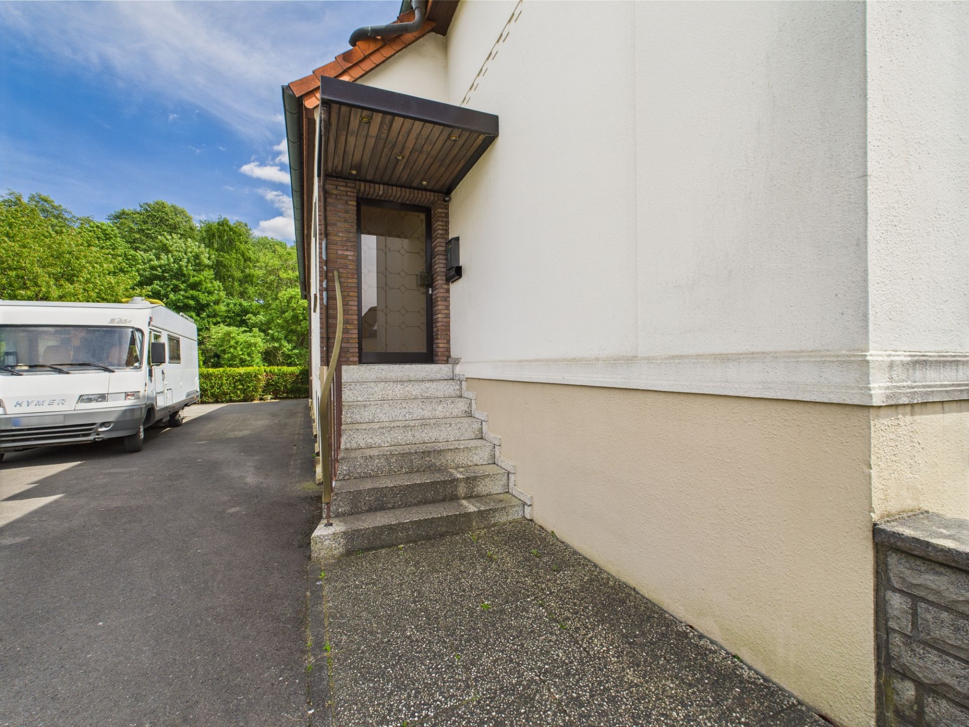 Außentreppe mit Geländer führt zu einer Haustür, daneben steht ein Wohnmobil.