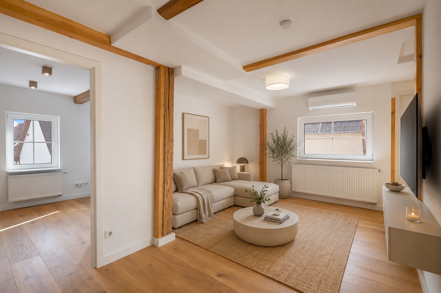 Helles Wohnzimmer mit Holzbalken, Sofa, Couchtisch, Teppich und Wandfernseher.