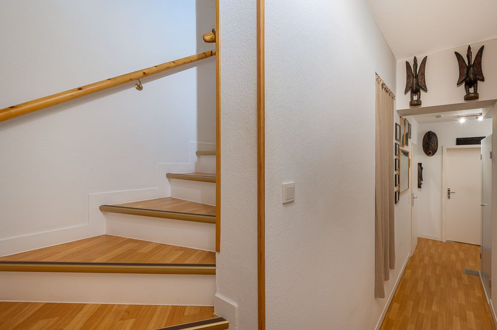 Heller Flur mit Holztreppe und Wanddekorationen in einem Wohnhaus.