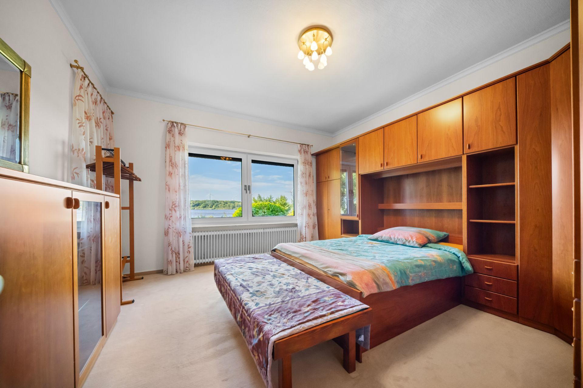 Schlafzimmer mit Doppelbett, Einbauschrank aus Holz und großem Fenster mit Blick nach draußen.