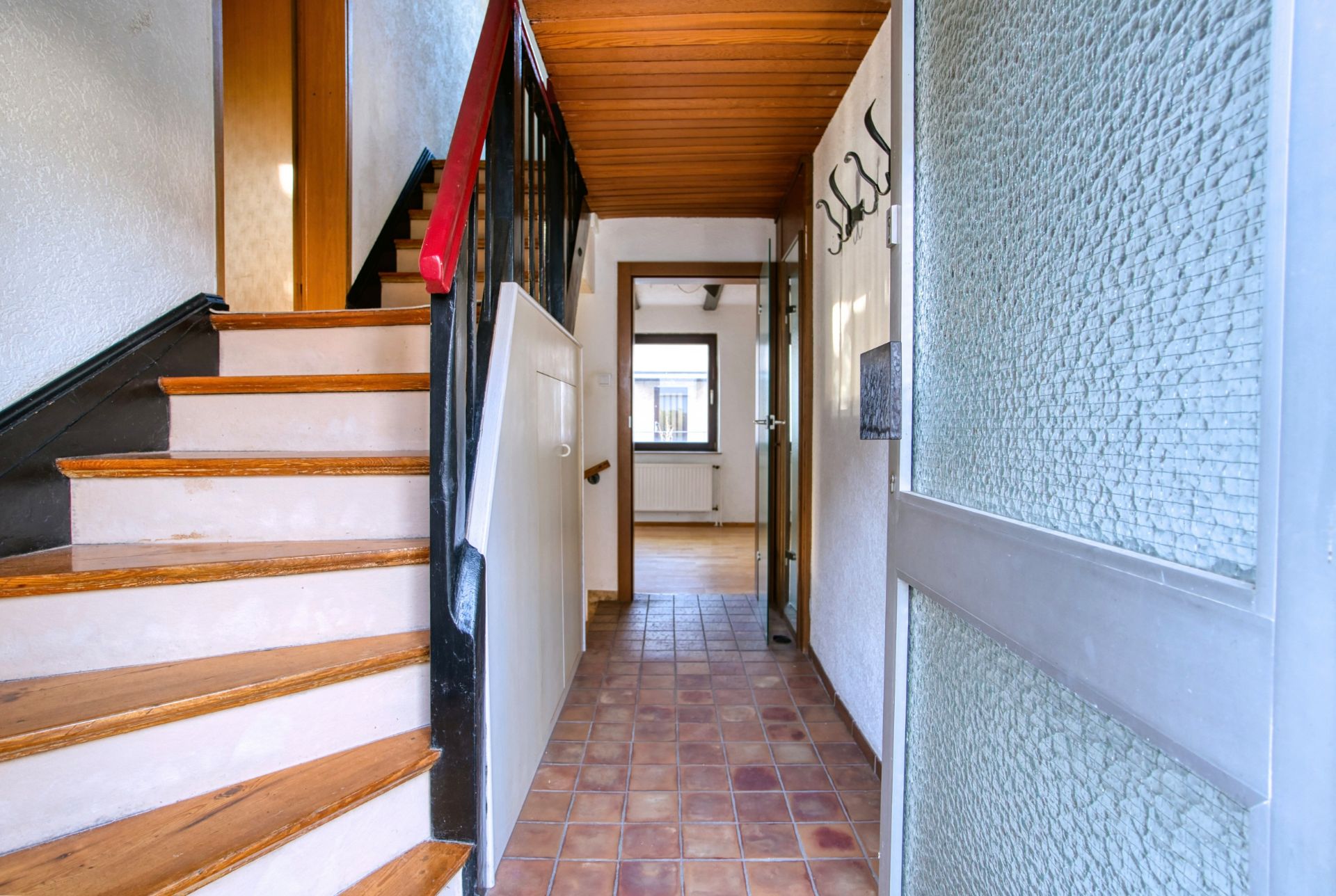 Flur mit braunen Fliesen, Treppe links und Garderobenhaken an der rechten Wand.