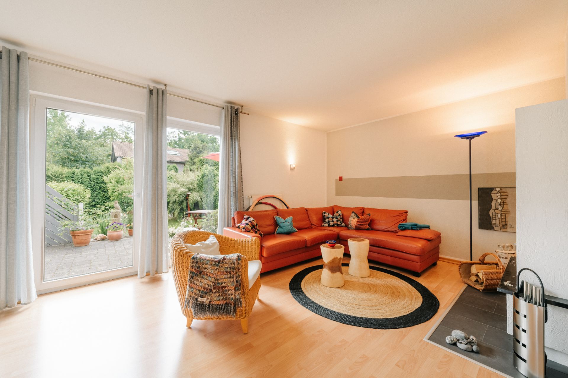 Helles Wohnzimmer mit rotem Ecksofa, Sessel, Teppich und Blick auf Terrasse und Garten.
